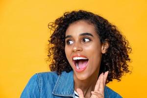 Fun close up portrait of young surprised African American woman with mouth open on studio yellow studio background photo