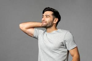 Portrait of young man smiling with hand behind neck, looking away and thinking after wake up, studio shot in isolated light gray background photo