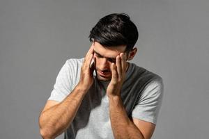 Fatigued young Caucasian man feeling headache, studio shot in isolated gray background photo