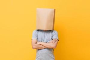 Concept portrait of Anonymous man with head covered with paper bag doing arms crossed gesture in yellow studio background photo