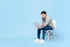 Portrait of smiling young handsome Caucasian man sitting while working on his laptop in isolated studio blue background photo