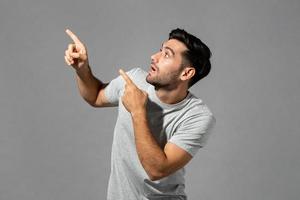 Shocked young Caucasian man gasping with hands pointing up isolated light gray studio background photo