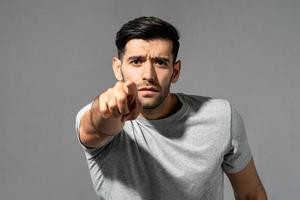 Young handsome Caucasian man looking and pointing finger at you in isolated light gray studio background photo