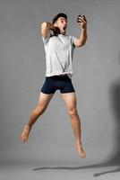 Full length portrait of shocked young Caucasian man in sleepwear waking up late looking at alarm clock and jumping in isolated gray studio background photo