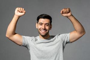 Young happy healthy Caucasian man smiling and raising his fists on isolated light gray studio background photo