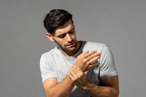 joven caucásico con dolor de muñeca, estudio filmado en un fondo gris aislado foto