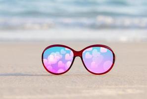 gafas de sol en la arena hermosa playa de verano y un corazón rosa para el día de san valentín foto