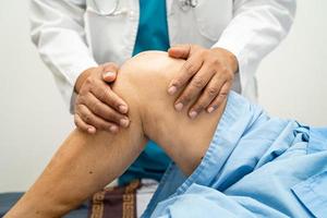 Asian doctor physiotherapist examining, massaging and treatment knee and leg of senior patient in orthopedist medical clinic nurse hospital. photo