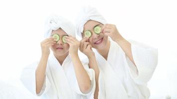 Happy beautiful mom and daughter in white bathrobe applying face mask in bedroom, Family and Beauty Concept. video