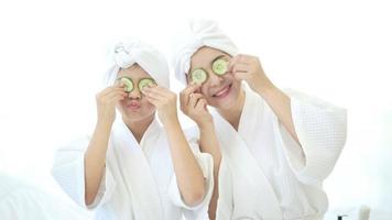 Happy beautiful mom and daughter in white bathrobe applying face mask in bedroom, Family and Beauty Concept. video