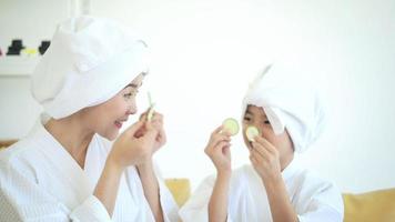feliz linda mãe e filha em roupão branco aplicando máscara facial no conceito de quarto, família e beleza. video