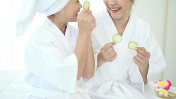 Happy beautiful mom and daughter in white bathrobe applying face mask in bedroom, Family and Beauty Concept. video