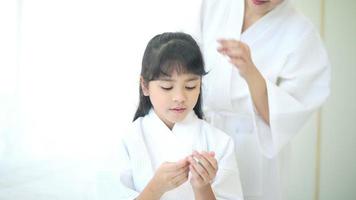 Happy beautiful mom in white bathrobe making her daughter hair at home, Family and Beauty Concept