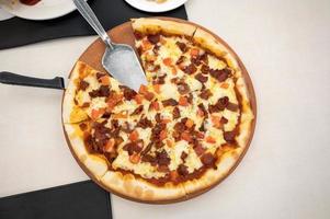 pizza casera con tocino, jamón y queso en una bandeja de madera foto