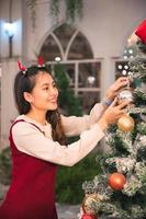 Asian woman wearing antler headband decorating ornament ball on christmas tree