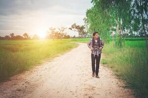 Young hipster man with backpack on his shoulder walking down countryside. photo