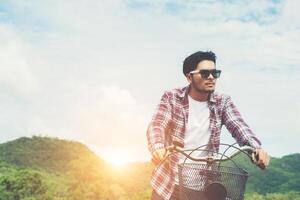 Young hipster man riding bike to the top of mountain enjoy with fresh breeze and nature behind the mountain view. photo