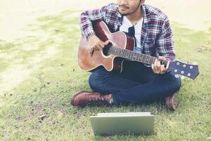 Young hipster man practiced guitar with laptop in the park,happy and enjoy playing guitar. photo