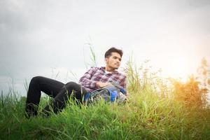 Young hipster man take a rest on the meadows after hiking, look away to find out another adventure. photo