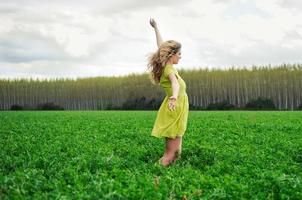 Beautiful blonde girl, dressed with a green dress, with open arms in a meadow photo