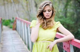 hermosa chica rubia, vestida con un vestido beige, de pie en un puente rural, con los ojos cerrados foto