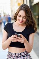 mujer joven enviando mensajes de texto con un teléfono inteligente en un entorno urbano foto