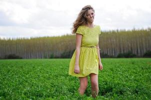 hermosa chica rubia, vestida con un vestido verde, de pie en un prado foto