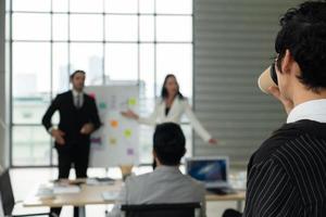 Young Woman Drinking Hot Coffee While Listening to Presentation of New Project in Meeting photo