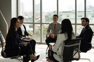 international business team including caucasian and asian people standing near window in office and discussing about project. diversity in business concept photo