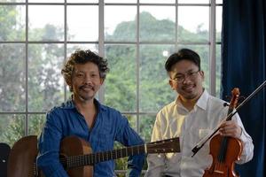 retrato de dos músicos asiáticos sonrientes que sostienen la guitarra y el violín foto