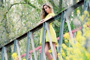 Beautiful blonde girl, dressed with a beige dress, standing in a rural bridge photo