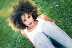 Young black woman with afro hairstyle sitting in urban park photo