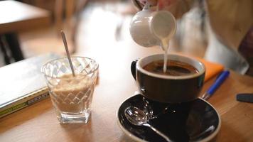 Frauenhand gießt Milch in eine Tasse schwarzen Kaffee - Nahaufnahme Tageslicht video