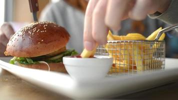 um homem comendo batatas fritas com ketchup de tomate e hambúrguer com verduras e camarão video