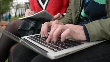 Estudiantes chicos y chicas con laptop en un banco en el parque escriben notas en un resumen