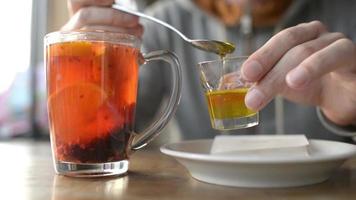 ein mann gießt honig in eine glastasse tee mit orange, beeren