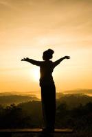 silhouette of free cheering woman open arms at mountain peak sunrise photo