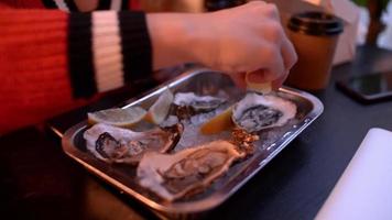 Young Woman sprinkles Fresh Oysters with Lemon Juice in the Restaurant Dinner
