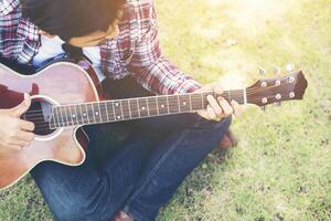 el joven hipster practicaba la guitarra en el parque, feliz y disfrutaba tocando la guitarra. foto