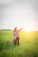 Young hipster couple standing on field pointing look away to the sky, couple in love. photo