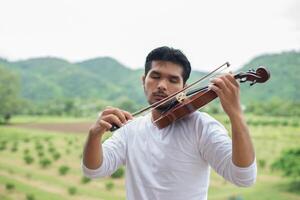 el joven músico hipster toca el violín en el estilo de vida al aire libre de la naturaleza detrás de la montaña. foto