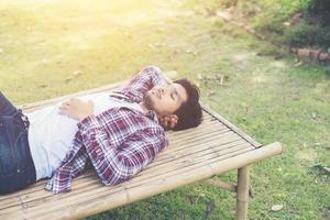 hipster joven feliz tumbado en un banco en el parque natural. foto