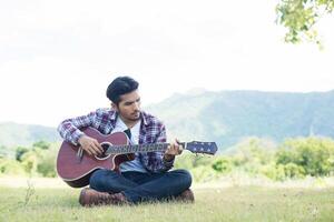 Young hipster man practiced guitar in the park,happy and enjoy playing guitar. photo