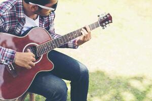 Portrait of young hipster man practiced guitar in the park,happy and enjoy playing guitar. photo