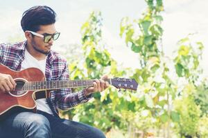 Portrait of young hipster man practiced guitar in the park,happy and enjoy playing guitar. photo