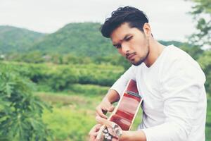 Young hipster man playing guitar to relaxing on his holiday, enjoy with natural and fresh air. photo