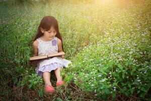 linda niña asiática leyendo un libro en la naturaleza. foto