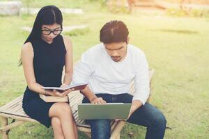 la joven pareja de educación sentada en el banco habla sobre estudiar al aire libre y el buen tiempo. foto