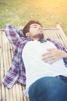 hipster joven feliz tumbado en un banco en el parque natural. foto