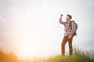 retrato de un joven hipster al aire libre levantando la mano con una mochila en el hombro, turismo de aventura. foto